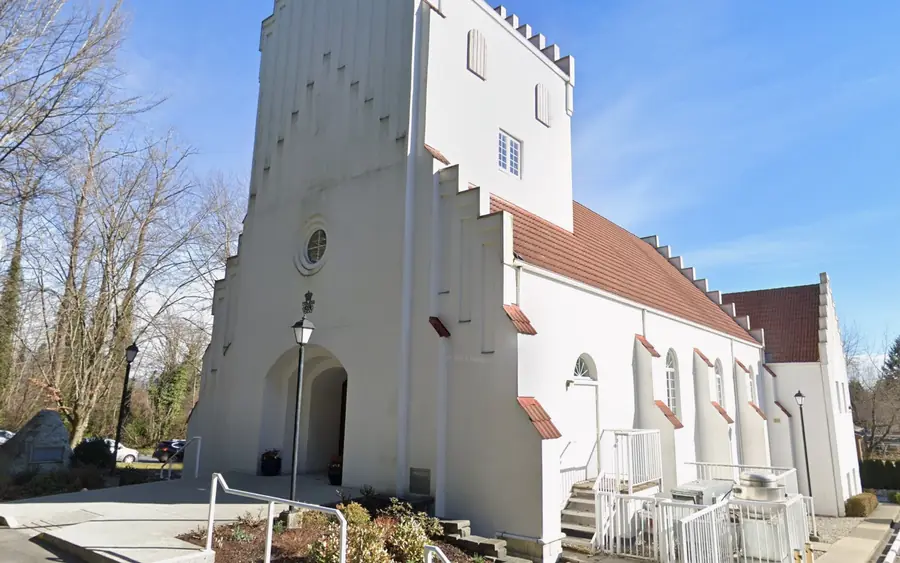 Exterior of a white church with a tall stepped bell tower in Burnaby, British Columbia.